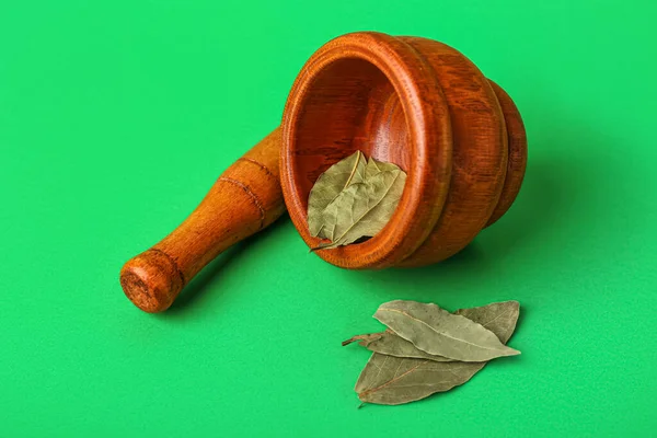 Wooden mortar and pestle with bay leaves on green background