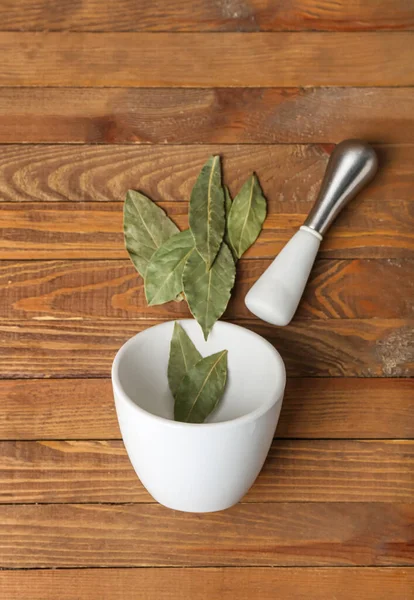 Mortar and pestle with bay leaves on wooden background
