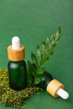 Yeşil arka planda bitki dalı ve yosun olan kozmetik yağı şişeleri.