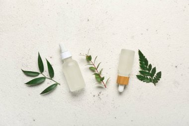 Beyaz grunge arka planında bitki dalları olan kozmetik yağı şişeleri.