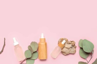 Kozmetik yağlı şişeler ve pembe arka planda okaliptüs dalı