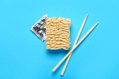 Çiğ erişteler, ahşap yemek çubukları ve mavi arka planda baharatlar.