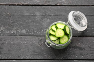 Koyu ahşap arka planda taze salatalık parçalarıyla dolu kavanoz.