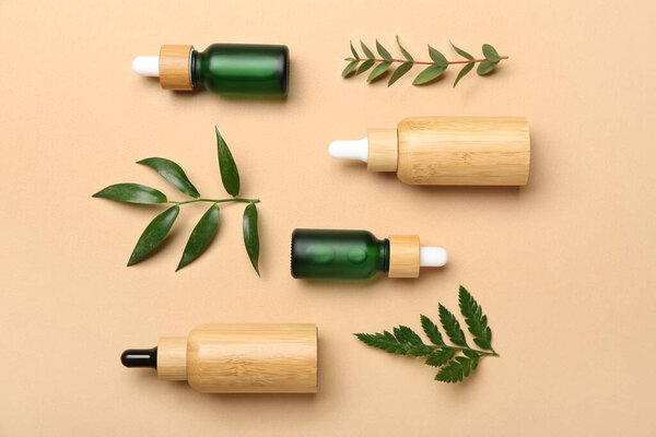 Бутылки косметического масла с растительными веточками на бежевом фоне