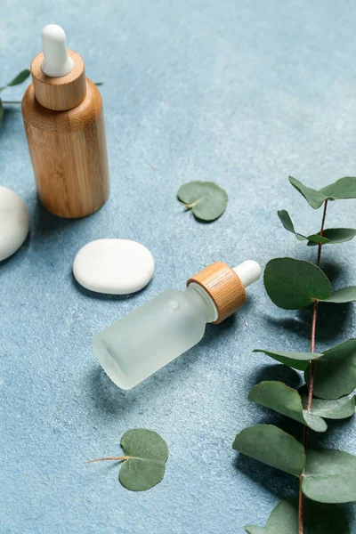 Butelki Olejkiem Kosmetycznym Gałązką Eukaliptusową Kamieniami Niebieskim Tle — Zdjęcie stockowe