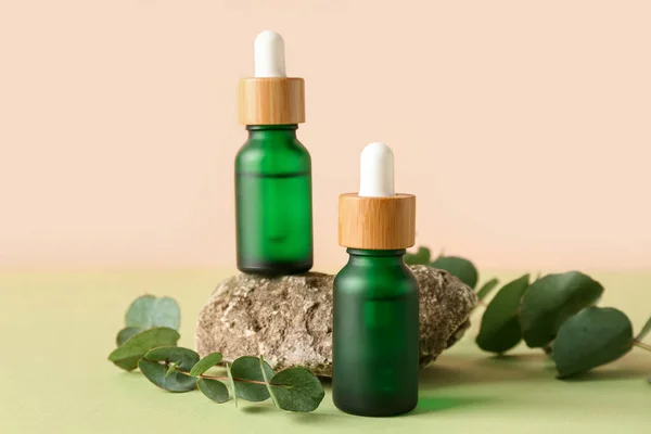 ユーカリの枝と緑のテーブルの上の石と化粧品油のボトル — ストック写真