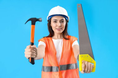 Yelekli ve mavi arka planda araçları olan kadın işçi