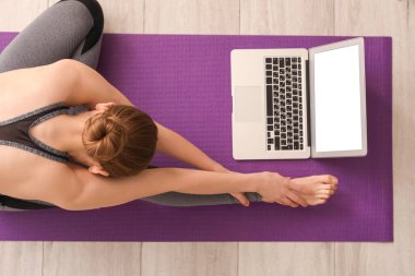 Dizüstü bilgisayarlı genç bir kadın spor salonunda yoga yapıyor.