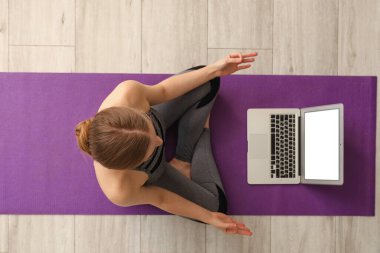 Dizüstü bilgisayarlı genç bir kadın spor salonunda yoga yapıyor.