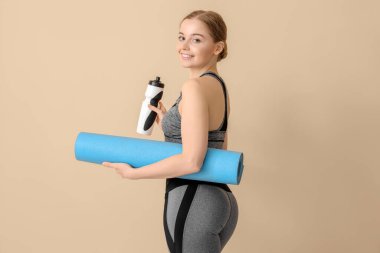 Yoga minderi ve bej arka planda bir şişe suyu olan genç bir kadın.