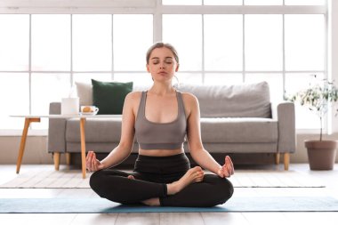 Sportif genç kadın evde meditasyon yapıyor.