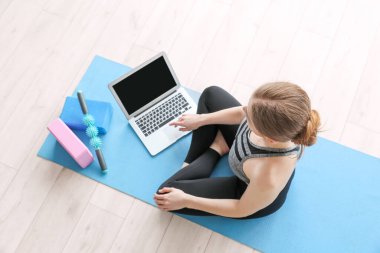 Dizüstü bilgisayarlı genç bir kadın spor salonunda yoga yapıyor.