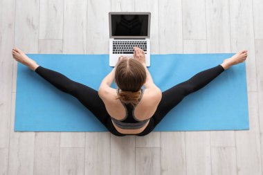 Dizüstü bilgisayarlı genç bir kadın spor salonunda yoga yapıyor.
