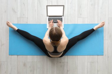 Dizüstü bilgisayarlı genç bir kadın spor salonunda yoga yapıyor.