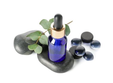 Kozmetik yağlı şişe, okaliptüs dalı ve beyaz arka planda taşlar