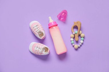 Bebek için bir şişe süt, çıngıraklı ve kalçaları leylak arkaplanlı