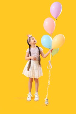 Sarı arka planda balonları olan taç giymiş küçük bir kız. Çocuk Bayramı kutlaması