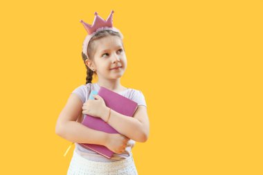 Sarı arka planda defterleri olan taç giymiş küçük bir kız. Çocuk Bayramı kutlaması