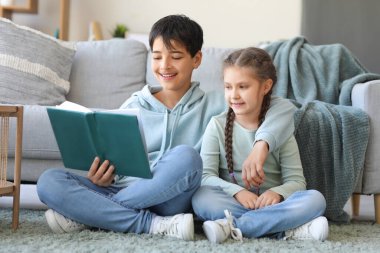 Kız kardeşi evde kitap okuyan küçük bir çocuk.