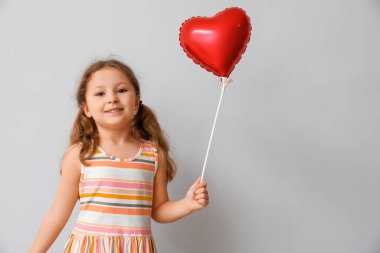 Işık arka planında kalp şeklinde balonu olan küçük bir kız. Çocuk Bayramı kutlaması