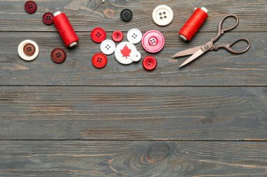 Akçaağaç yapraklı düğmeler, iplik makaraları ve makaslar koyu ahşap arka planda. Kanada bayrağı konsepti