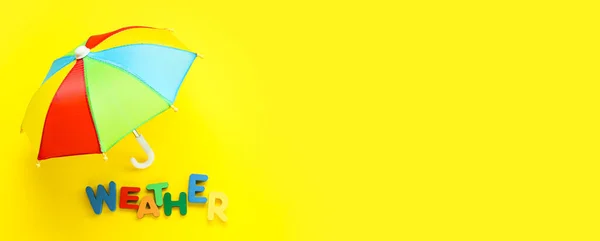 Rainbow umbrella and colorful word WEATHER on yellow background with space for text