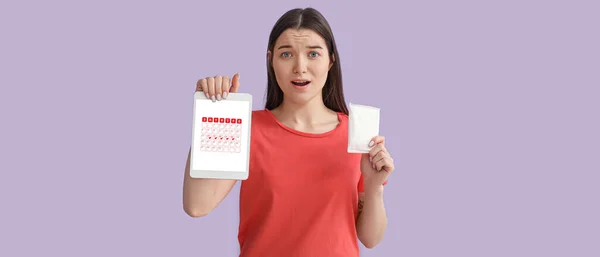 惊慌失措的年轻女子拿着月经垫和平板电脑 屏幕上有开放的日历 背景是紫丁香 — 图库照片