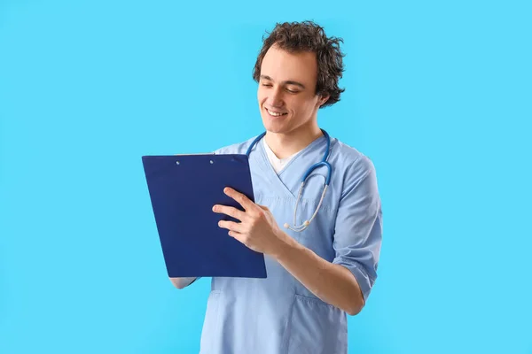 在蓝色背景的剪贴板上书写的年轻医生 — 图库照片