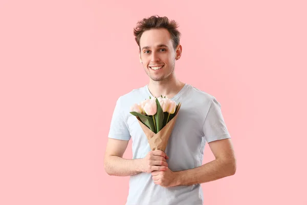 Young man with bouquet of tulips on pink background