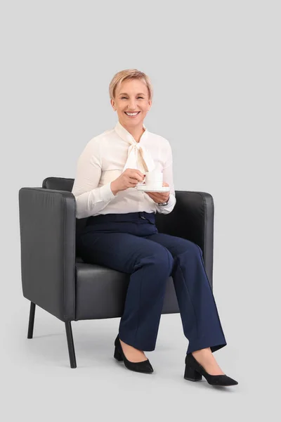 Reife Geschäftsfrau Trinkt Kaffee Während Sie Sessel Vor Grauem Hintergrund — Stockfoto