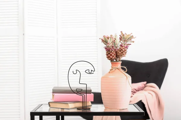 Vase with baby pineapples, books and decor on table in living room