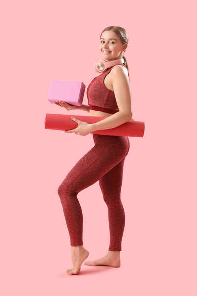 Sporty young woman with mat and block for yoga on pink background