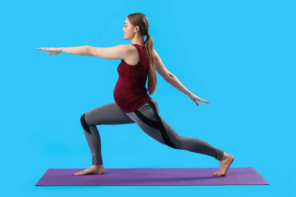 在蓝色背景下做瑜伽的年轻孕妇 — 图库照片