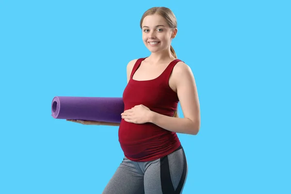 stock image Pregnant young woman with yoga mat on blue background