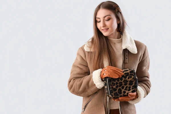 stock image Beautiful young woman in leather gloves, sheepskin and with modern bag on light background