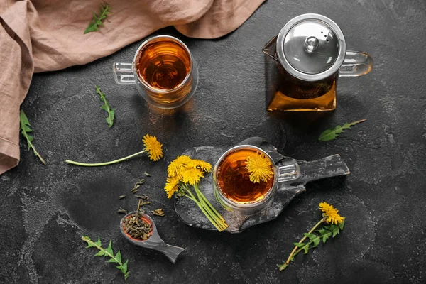 stock image Glass cups of healthy dandelion tea and teapot on black background