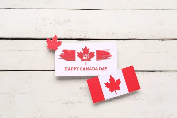 Card with text HAPPY CANADA DAY, date 1 JULY 1867 and flag on white wooden background