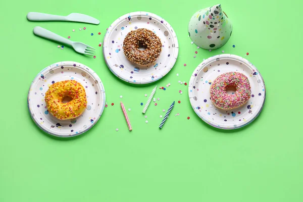 stock image Paper disposable tableware with donuts, party hat and candles on green background