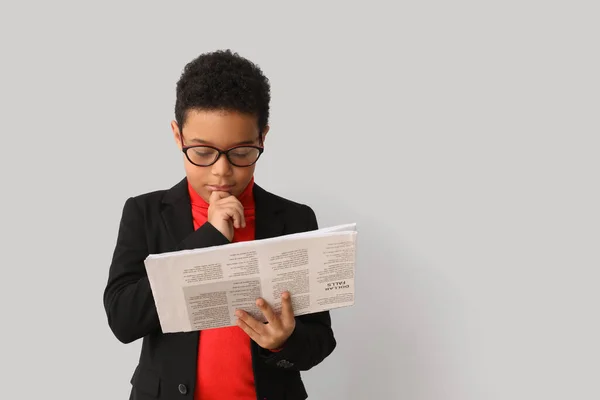 stock image Little African-American boy reading newspaper on light background. Children's Day celebration