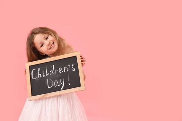 小女孩拿着粉红背景的印有儿童节字样的黑板 — 图库照片