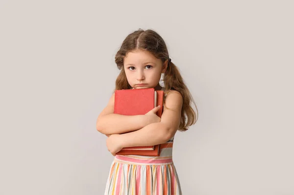 Little girl with books on light background. Children\'s Day celebration