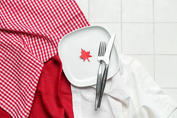 Table setting with paper maple leaf on white tile background. Canadian flag concept