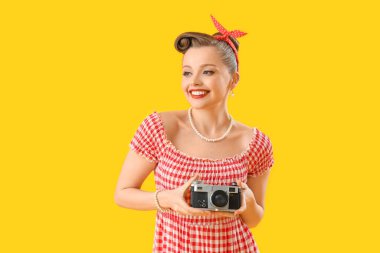 Young pin-up woman with photo camera on yellow background