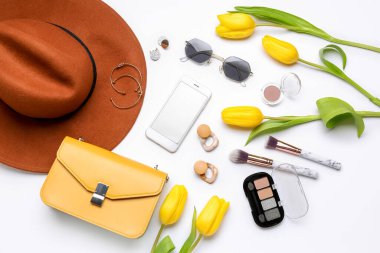 Beyaz arka planda modern cep telefonu, kozmetik ürünleri, aksesuarlar ve lale çiçekleriyle kompozisyon