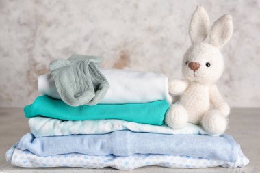 Bebek kıyafetleri ve arka planda oyuncak tavşan yığını.