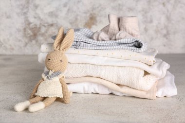 Bebek kıyafetleri yığını ve arka planda örülmüş oyuncak tavşan.