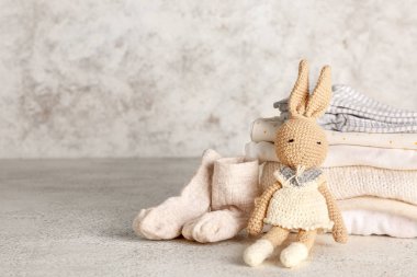 Bebek kıyafetleri yığını ve arka planda örülmüş oyuncak tavşan.