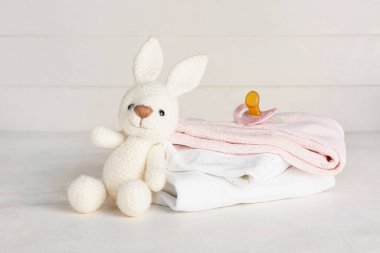 Bebek kıyafetleri, oyuncak tavşan ve emzik yığını.