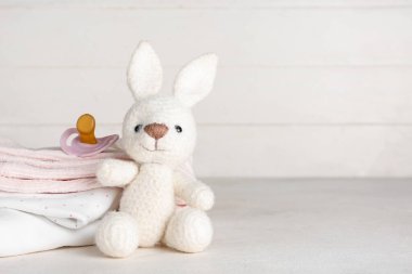 Bebek kıyafetleri, oyuncak tavşan ve emzik yığını.