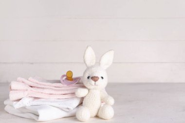 Bebek kıyafetleri, oyuncak tavşan ve emzik yığını.